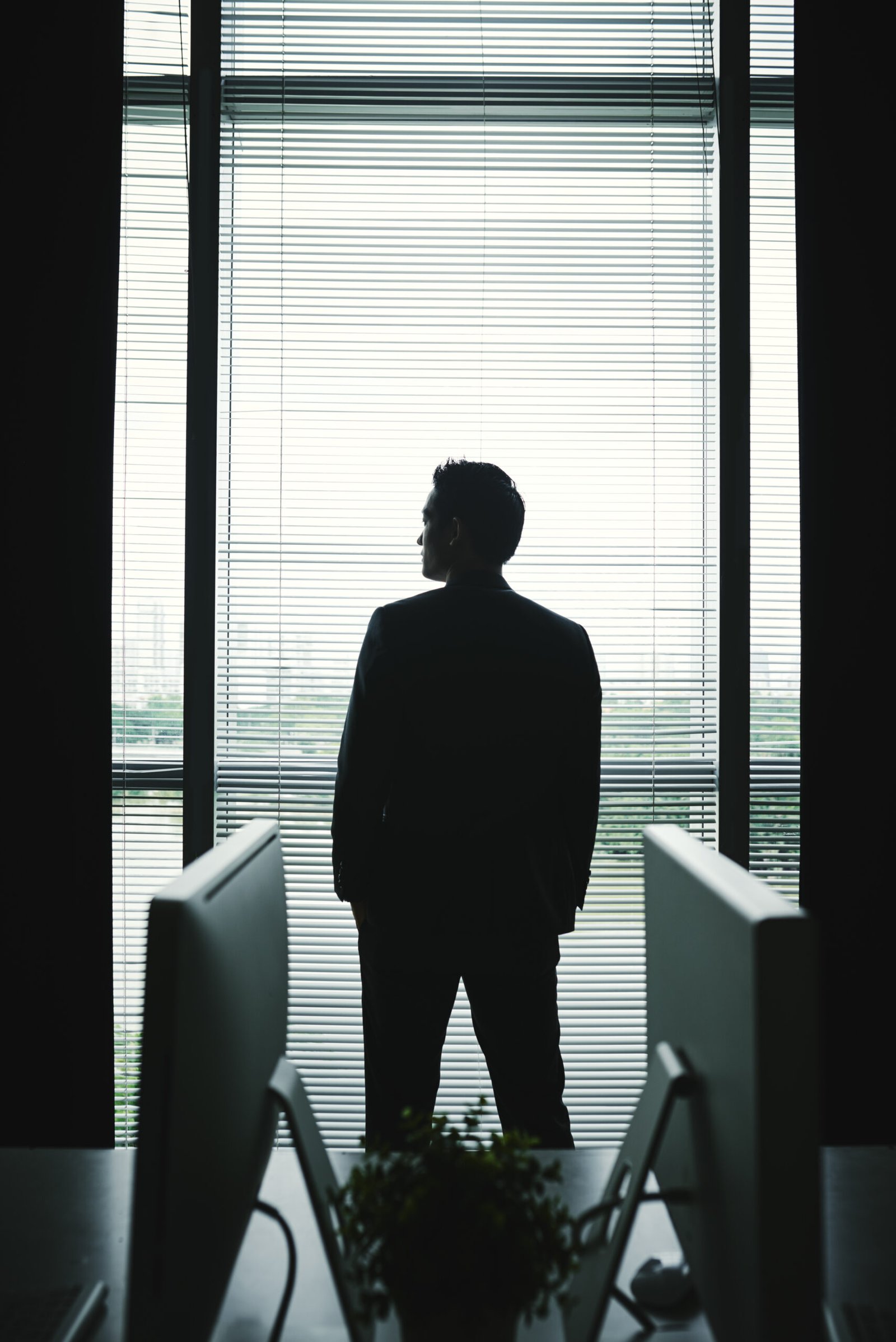 Confident ambitious businessman looking through the window of his office, view from the back